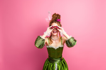 Elegant young woman in vivid green baroque costume posing joyfully against a bright pink background, exuding vintage aristocratic charm