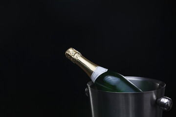 Bottle of champagne in bucket on black background, space for text