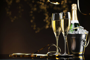 Champagne and bucket of ice on mirror surface against brown background with blurred lights, space for text