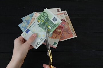 Wall Mural - Woman cutting euro banknotes at black wooden table, closeup