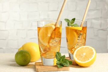 Wall Mural - Refreshing iced tea with drinking straws, mint, lemon and lime on light textured table against grey background, closeup