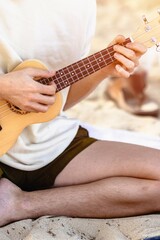 young caucasian male playing ukulele on beach sand in casual attire