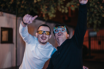 Poster - Two happy individuals enjoying a lively celebration outdoors, wearing colorful glasses and expressing excitement, showcasing the joy of fun gatherings during festivities.