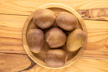 Wall Mural - Several ripe kiwis in a wooden plate on a wooden table, close-up, top view.