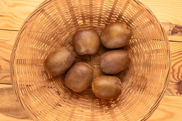 Wall Mural - Several ripe kiwis in a straw plate on a wooden table, close-up, top view.