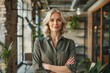 © darshika - Confident mature businesswoman with arms crossed, standing in a modern office.