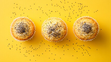 Wall Mural - Three golden-brown lemon poppy seed muffins arranged in a neat row on a pastel yellow background, with scattered poppy seeds around them