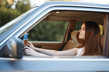 Wall Mural - Young woman with long hair driving a vintage car outdoors, showcasing confidence and relaxation in a serene environment.