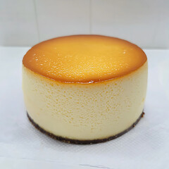 Poster - Golden-topped cheesecake with a dark crust sits on a white surface, its smooth texture and simple form appealing.