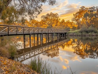 Wall Mural - Golden sunset reflects on calm river, wooden bridge, autumn trees.