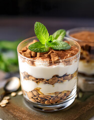 Sticker - Layered dessert in a glass, topped with cocoa and mint, sits on a wooden board with a blurred background