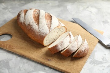 Wall Mural - Wooden cutting board with fresh bread and knife on grey table, closeup