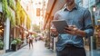 © Photock Agency - Young man using tablet in modern urban setting with afternoon sunlight and greenery