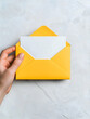 © Pukan - A hand holds a bright yellow envelope with a white letter inside, set against a light textured background.