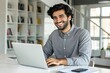 © antusher - Smiling young man working on laptop in modern office