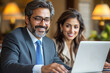 © Chatchaa - A professional man and woman collaborate on a laptop, smiling in a cozy, well-lit environment, showcasing teamwork and modern business interaction.