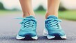 © Manon - A pair of vibrant blue running shoes on a person's feet, set against a blurred outdoor background, ready for exercise or jogging.