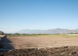 Photo of an empty field. Flat landscape with dirt field and blue sky background,