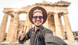 © Davide Angelini - Happy tourist visiting the Acropolis of Athens, Greece - Smiling traveler man taking selfie picture with smart mobile phone outdoors