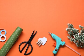 Wall Mural - Hot glue gun and handicraft materials on orange background, flat lay. Space for text