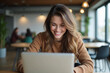 © yulya - A smiling young woman using a laptop in a modern coworking space