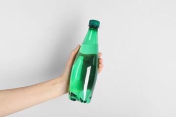 Wall Mural - Woman holding plastic bottle of water on light background, closeup