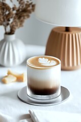 Wall Mural - Latte art in ribbed glass on metal coaster against white background with minimal decor elements. Cozy coffee moment with gradient foam and leaf pattern.