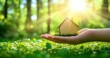 © galendra - Small wooden house model in a hand, surrounded by grass, with sun shining.