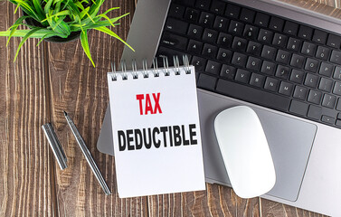 Tax deductible text on a notepad with a laptop, pen, and plant on a wooden desk