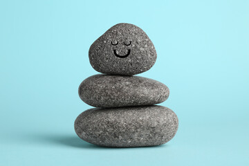 Wall Mural - Stack of rocks with drawn smiley face on light blue background. Harmony and life balance