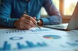 © miss irine - Close-up of man reviewing graphs, diagrams with pen near laptop. Financial analyst examines business reports, performance analysis, investment data, company sales statistics. Manager plans project,