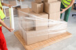 © Pixel-Shot - Male loaders wrapping boxes on pallet with stretch film in warehouse
