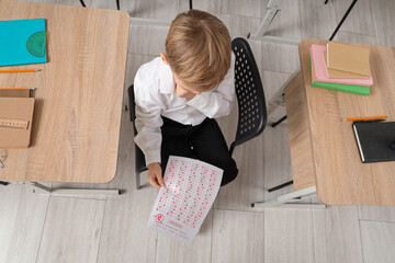 Wall Mural - Thoughtful schoolboy with results of test sitting in classroom, top view