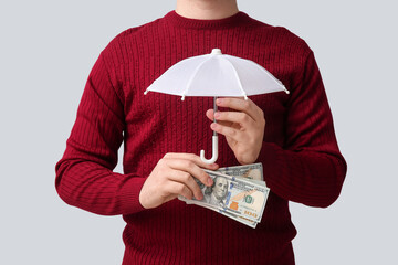 Wall Mural - Man with money and toy umbrella on light background, closeup