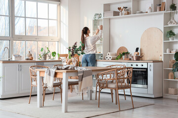 Wall Mural - Young woman near shelf unit in dining kitchen, back view