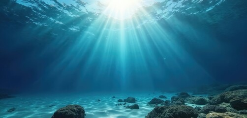 Wall Mural - Sunlight streams into deep blue ocean creating undersea scene with rocks on bottom. Rays of light penetrate clear turquoise water surface with ripple, diving depth. Sunbeam beams through liquid