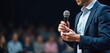 Presenter with mic on stage speaks to audience in hall. Motivational speaker gives speech at conference. Businessman presents report at summit. Public performance in auditorium.