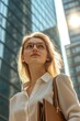 © Prakakrong - A young businesswoman standing outside a skyscraper, holding a briefcase and looking confident, sunlight reflecting on modern architecture, corporate lifestyle