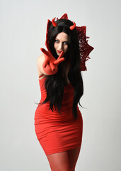 Wall Mural - portrait of beautiful dark haired model wearing elegant red dress with gothic fantasy burlesque halloween themed devil costume, with horns. isolated pose on white studio background