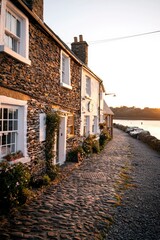 Wall Mural - Quaint stone cottages line a cobblestone path leading to a tranquil lake at sunset