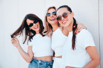 Wall Mural - Three young beautiful smiling hipster female in trendy summer white t-shirt  and jeans clothes. Sexy carefree women posing in street. Positive models having fun, going crazy. In sunny day, sunglasses