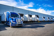 © vit - Big rig blue semi truck with refrigerator semi trailer standing in row with another semi trailers in warehouse dock gates loading cargo for the next freight