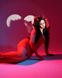 © faestock - portrait of beautiful  female pin-up model wearing red dress with gothic fantasy burlesque halloween themed devil costume, horns & gloves. isolated sitting pose, dramatic colourful studio lighting