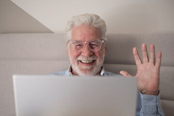 Wall Mural - Smiling handsome caucasian senior bearded man with eyeglasses lying on bed using computer, elderly retiree browsing internet by laptop