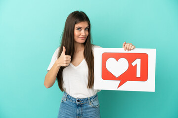 Wall Mural - Young caucasian woman isolated on blue background holding a placard with Like icon with thumb up