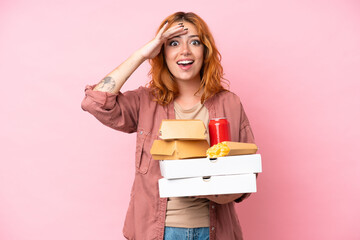 Young caucasian woman holding fast food isolated on pink background with surprise expression