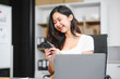 © R Photography - An Asian businesswoman works at her desk office, smiling while analyzing financial data planning business strategies on her laptop to enhance profitability,optimize resources,ensure financial growth