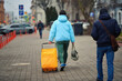 © Tricky Shark - Traveler in blue jacket walks down the city sidewalk with yellow suitcase, embracing journey ahead on cold winter day. Man with rolling suitcase and bag in hand walks through the streets, back view
