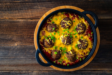 Wall Mural - Cowboy meatballs baked with cheddar cheese in frying pan on wooden table