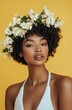 © thiquynh - A beautiful woman with short, curly hair, wearing a white halter top and a floral wreath on her head, against a yellow background.